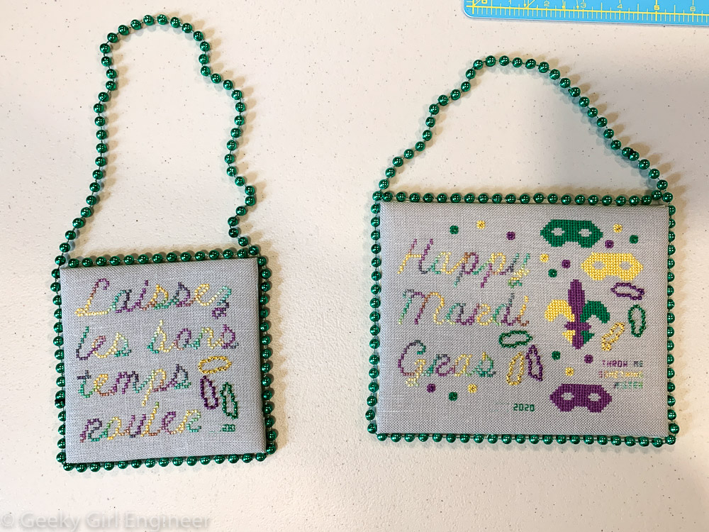 Cross-stitch pieces on padded mat board hung by Mardi Gras pieces